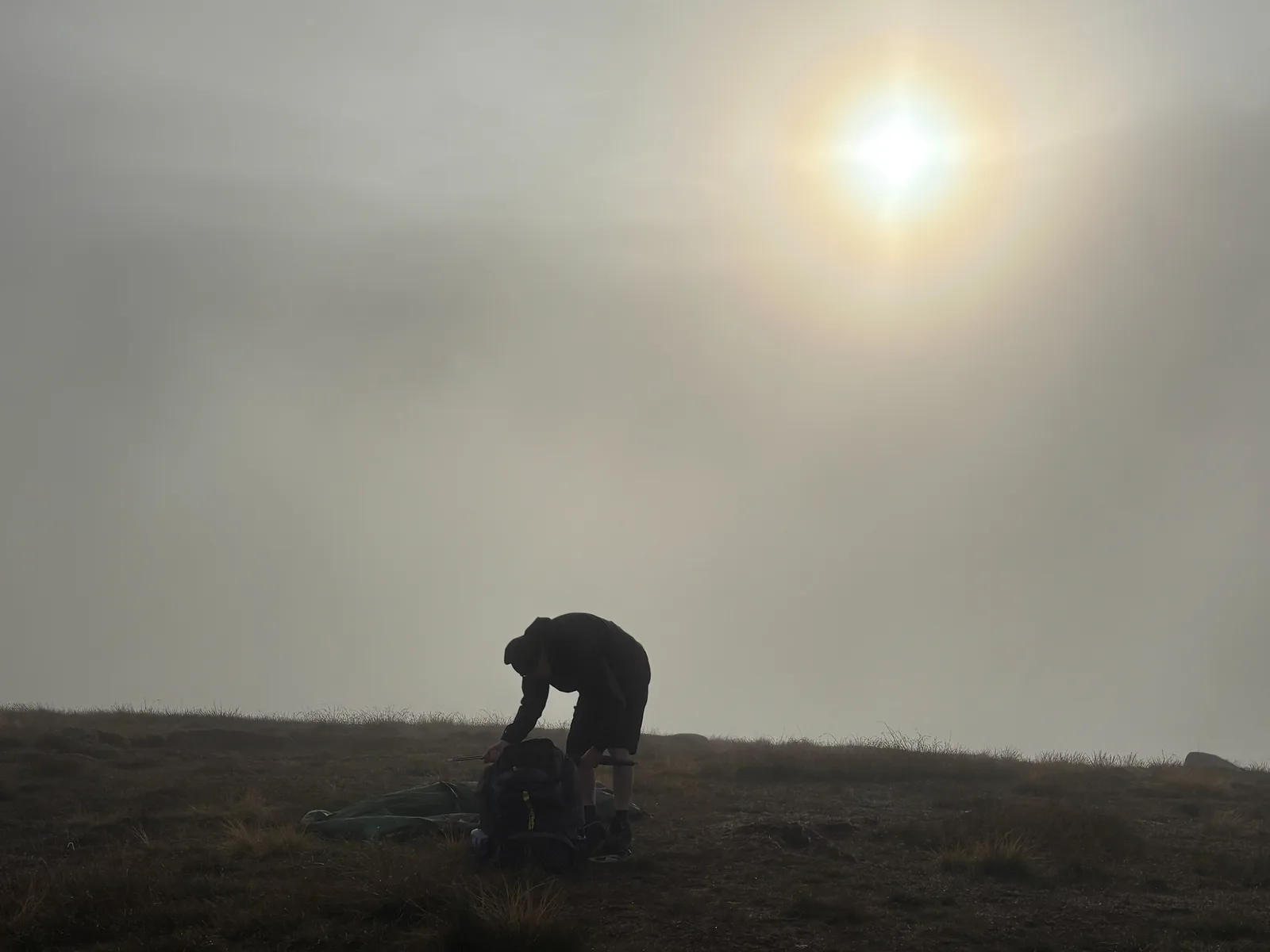Breaking camp on the summit as the sun burns through the clag after a wild camp at Lough Shannagh